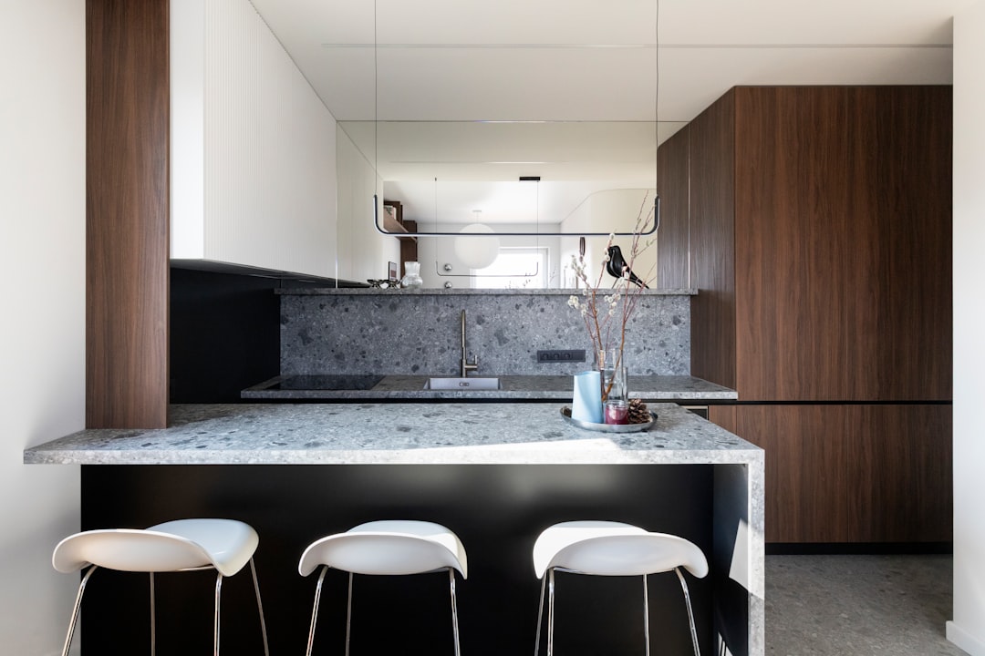 The material palette is restrained and consistent throughout the apartment: Dark-stained wood cabinetry defines the kitchen and storage volumes Grey terrazzo surfaces form the kitchen island and backsplash White walls and ceilings provide a neutral background, enhancing natural light Warm-toned wooden flooring unifies the space